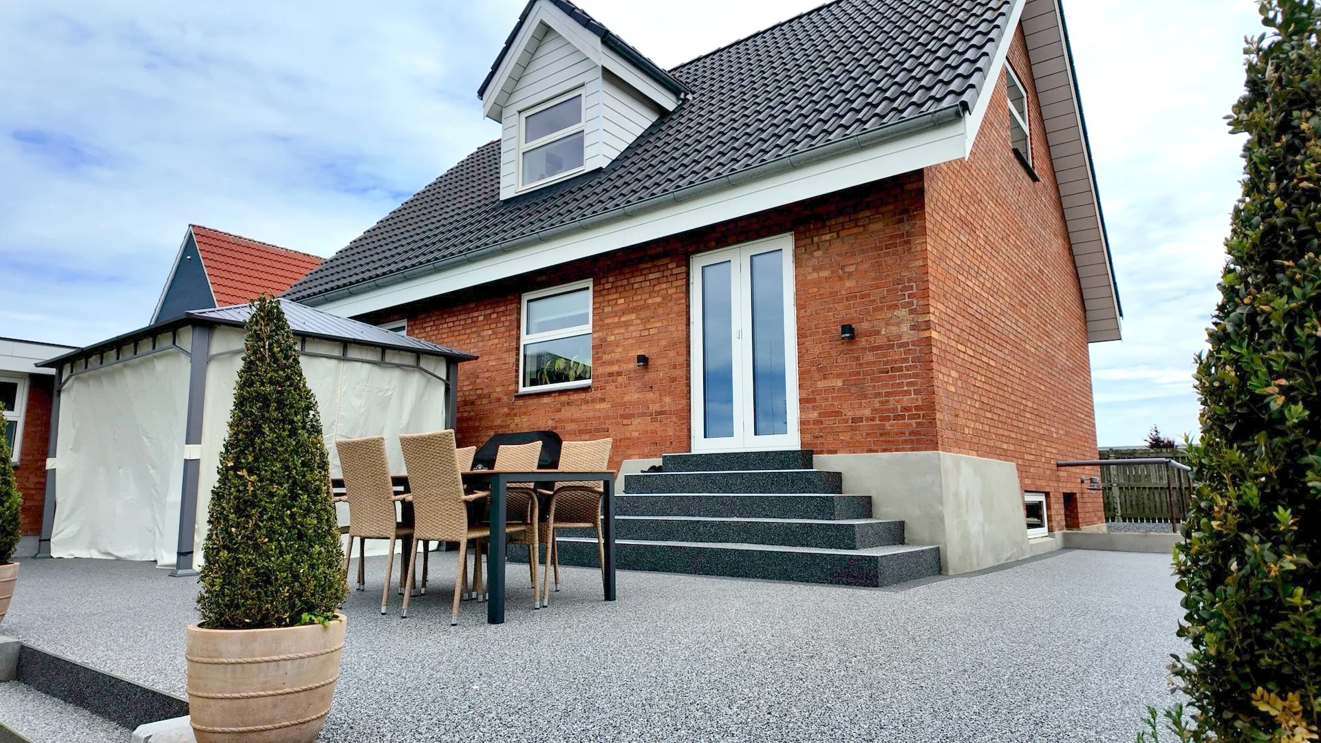 Færdig resin-bound stenbelægning omkring rødstenshus med terrasse, granittrappe og havemøbler