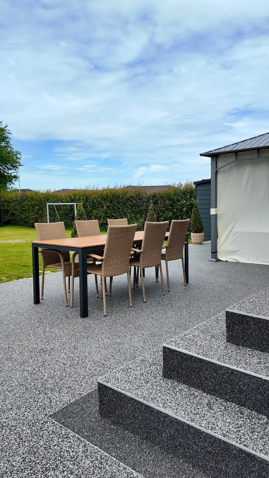 Terrasse i helstøbt stenbelægning med spisebord, stole og granittrappe